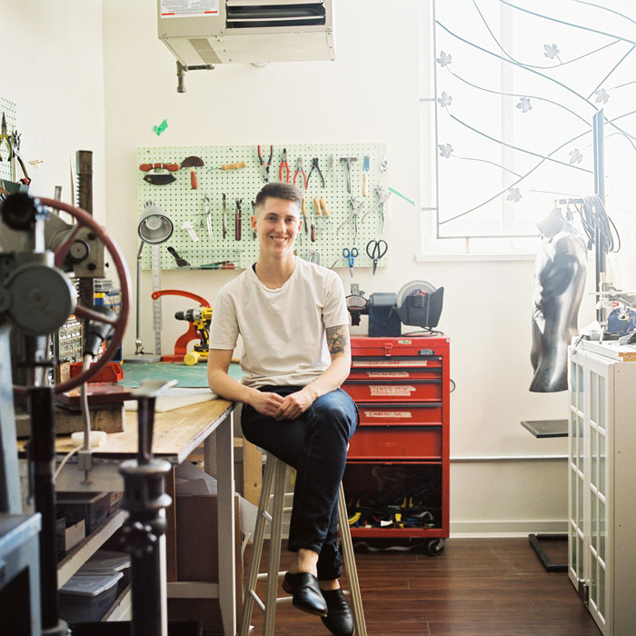 Ariss Grutter, a light-skinned nonbinary person with short brown hair at a workbench in their East Van leatherworking shop.