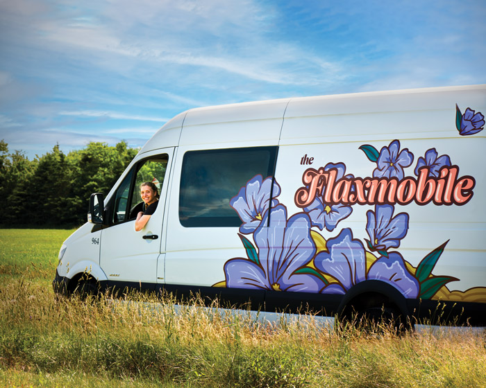 Jennifer Green smiles out the driver's side window of a white van painted with purple flowers and the word "Flaxmobile."