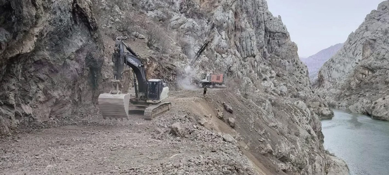 Two excavators carve a road through a rocky mountain gorge above a river in Iraqi Kurdistan.